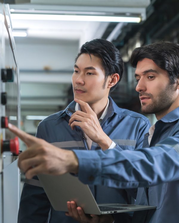Male Asian caucasian engineer professional having a discussion standing consult at machine in the factory ,two expert coworker brainstorm explaining and solves the process of the cnc operate machine